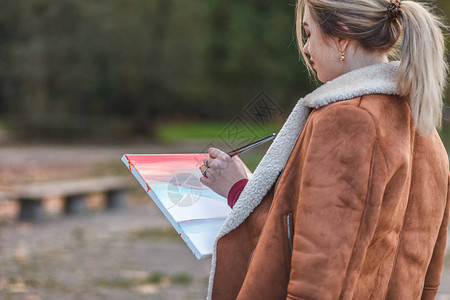 身穿棕色夹克的女画家站在公园里图片