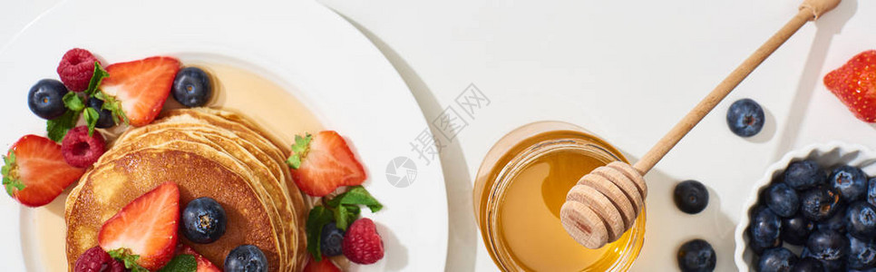 在大理石白色表面的盘子上放着蜂蜜蓝莓和草莓的美味煎饼的顶视图片
