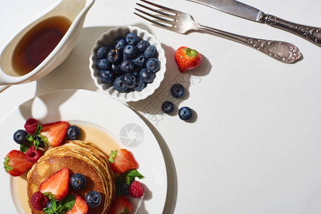 在靠近餐具的盘子上放着蓝莓和草莓的美味煎饼的顶视图图片