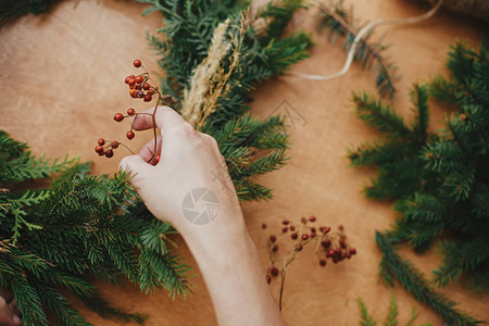 手拿着浆果和冷杉树枝松果木桌上的线圣诞花环工作坊正宗时尚的静物制作质图片