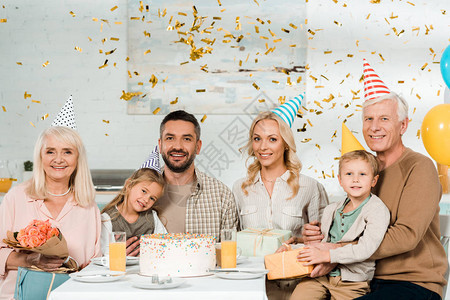 幸福的家庭坐在厨房桌边接近生日蛋糕的时候掉下彩蛋和图片