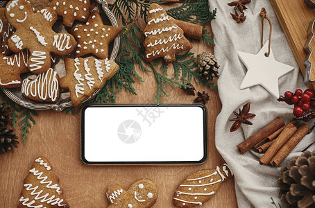 电话与空屏幕和节日姜饼干与茴香肉桂松果雪松树枝在质朴的桌子上图片