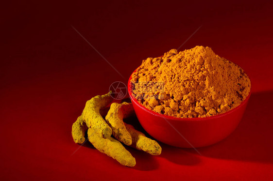 红色背景中红碗中的干姜黄粉和根或树皮图片