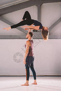 杂技瑜伽和瑜伽姿势的主题一对两男一女站在体位的置那家伙用伸出的手臂把女孩高地拱起来在有工作室背图片