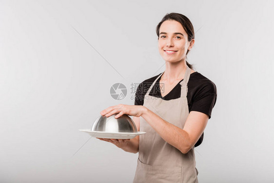 穿着围裙的快乐年轻的黑发女服务员在单独地站在镜头前时手贴着Clo图片