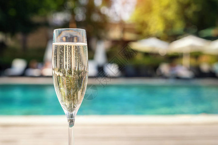 度假期间在豪华度假酒店的池畔特写白色香槟或普罗赛克玻璃与上升的气泡的起泡酒与室外的蓝色水池背景清背景图片