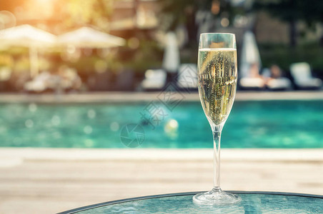 度假期间在豪华度假酒店的池畔特写白色香槟或普罗赛克玻璃与上升的气泡的起泡酒与室外的蓝色水池背景清背景图片