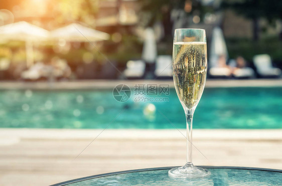 度假期间在豪华度假酒店的池畔特写白色香槟或普罗赛克玻璃与上升的气泡的起泡酒与室外的蓝色水池背景清图片