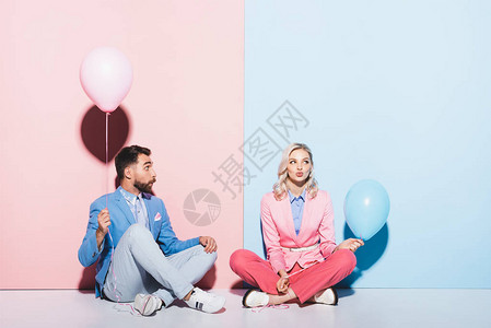 迷人的女人和震惊的男子拿着粉红和蓝底气球在粉色图片