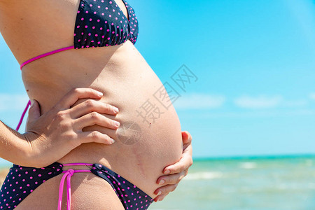一个怀孕的女孩在海边的沙滩上双手托着大肚子图片