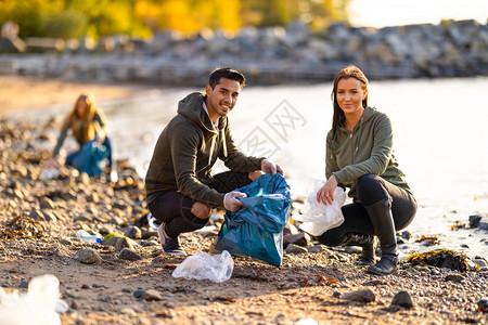 微笑的多民族环保志愿者清洁海滩的画像年轻的男人和女人在阳光明媚的日子里蹲着他图片