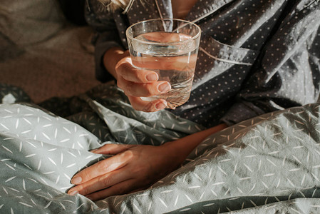 躺在床上的女人手里拿着一杯水快乐的早晨穿着睡衣的女孩健康的生活方式图片