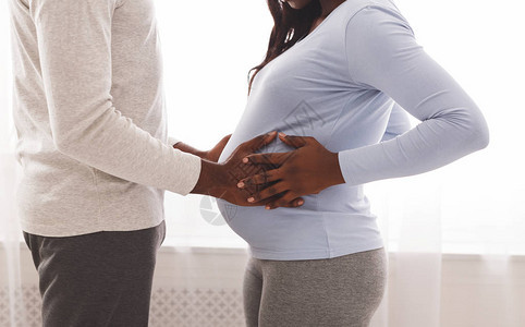 非洲男人在家里的窗户背景上抚摸怀孕的妻子腹部图片