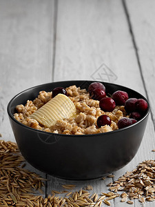 健康的早餐燕麦片配小红莓和黄油黑色杯粥白色木制背景上燕麦粒散落在图片