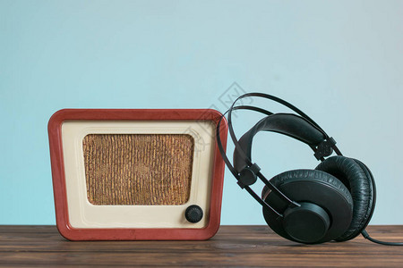 蓝色背景的木制桌子上的古老无线电和耳机图片