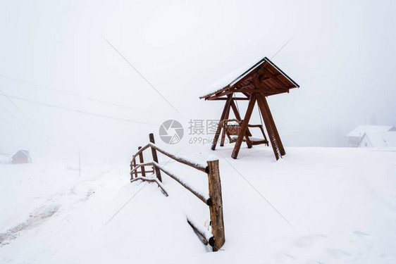 雾中雪山村的木栅栏和秋千图片