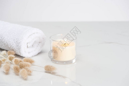 在玻璃中烧白蜡烛和大理石白色表面的毛巾上图片
