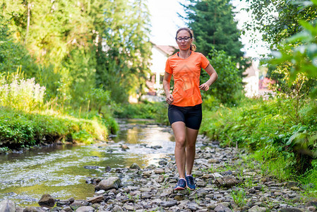 穿着明亮橙色T恤的女孩沿着山河奔图片