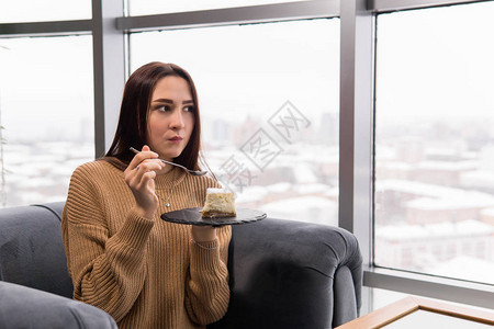 冬天女孩坐在大窗户前的椅子上吃芝士蛋糕图片