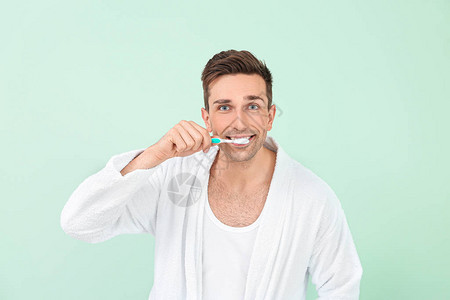 穿着浴袍的帅哥在彩色背景上清洁牙齿图片