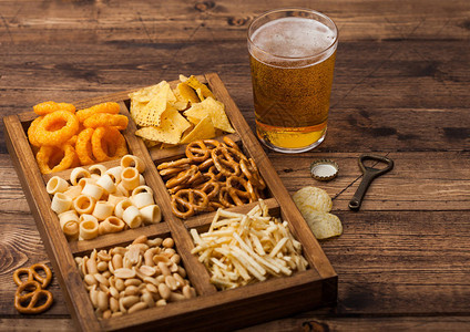 杯工艺啤酒和开瓶器与木背景上的零食盒图片