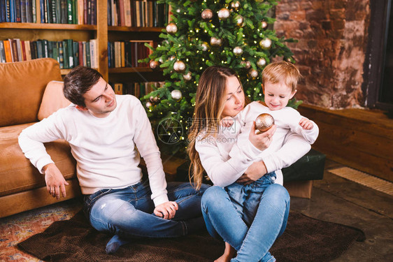 家庭圣诞节概念可爱的家庭在冬天的晚上坐在圣诞树附近有儿子的幸福家庭在沙发附近的地板上在家庭在时间在家庭图片