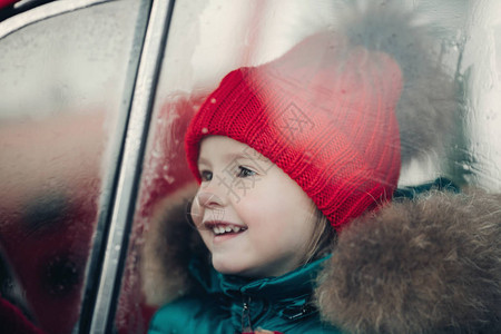 戴着红色帽子的可爱冬季女孩微笑着坐在车里玩中景图片