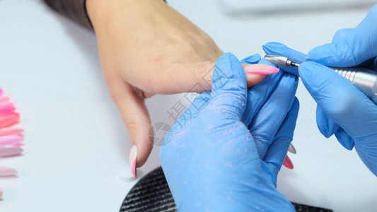 特写美甲沙龙的电动指甲钻在美容院进行硬件修指甲女美甲师从客户指甲上去除旧凝胶吸风格栅在美容院的指图片