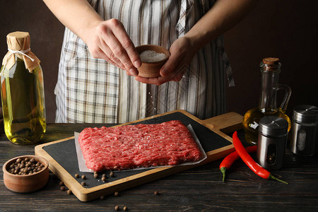 女人用香料在木桌上的碎肉上撒盐特写图片