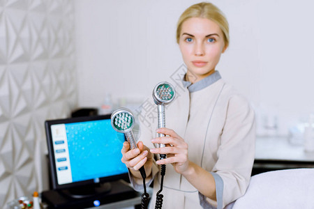 金发美女医生美容师和美容师手持美塑疗法LED光子疗法射频皮肤再生工具图片