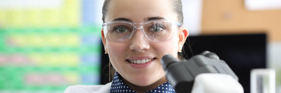 化学家的特写镜头微笑着拿医疗材料好看的女实验室工作人员和现代显微镜科学背景图片