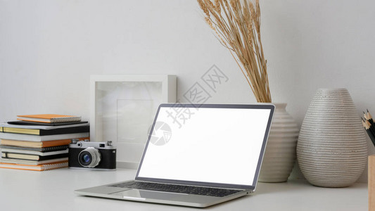 在白墙背景的白桌上用空白屏幕笔记本电脑相机框架书籍和装饰品拍摄图片