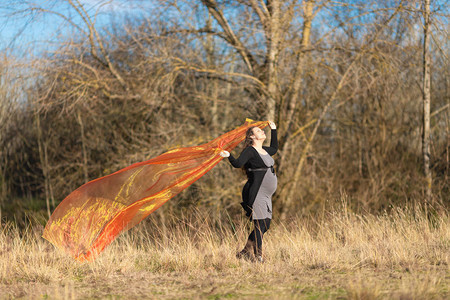 公园中的孕妇带着橙色丝绸围巾在风中挥舞图片