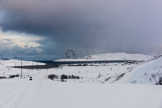 积雪覆盖的冬季道路通往俄罗斯科拉半岛北极圈上方最北端海上的一个小渔村路上的图片