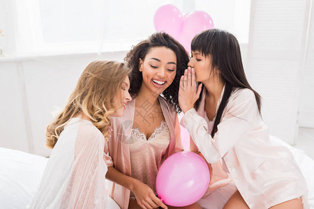 快乐的多文化女友在床上用粉色气图片