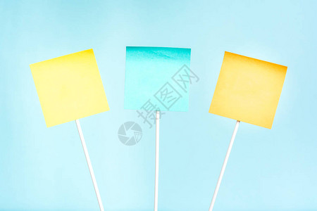 三张黄色蓝色和橙色纸笔粘贴在棍子和蓝背景上空图片