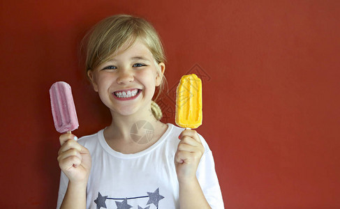 在红色背景上吃冰淇淋的金发小女孩图片