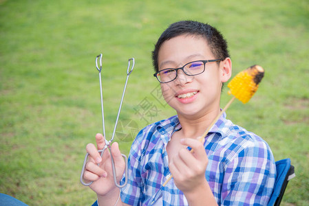 年轻小男孩拿着烤甜玉米在图片