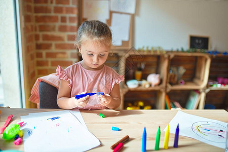 在幼儿园用彩色铅笔绘画的美丽的金发小图片