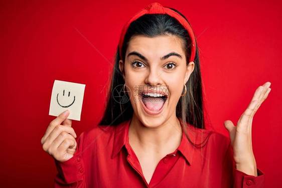年轻漂亮的黑发女人拿着带有微笑表情符号的提醒纸图片