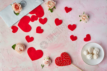 粉红色背景上的多个红心糖果花头信封情人节的概念顶视图图片