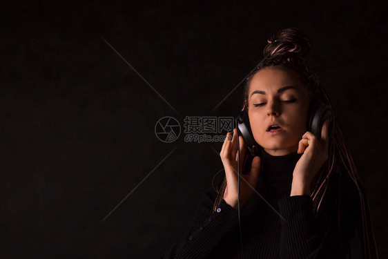 一个拥有大耳机和猪尾Zizi的女孩在黑背景上闭着眼睛收听音乐给传单和标语放文字图片