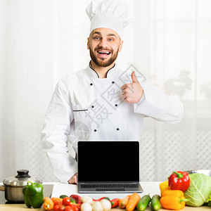专业厨师用空屏幕控制手持笔记本电脑的盖伊专业主厨在厨房站图片