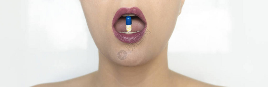 一个漂亮的女人在她的牙齿之间夹着一颗药丸一种抗生素一种解热镇痛药用红色唇膏的美丽妆容治疗和预防冠图片