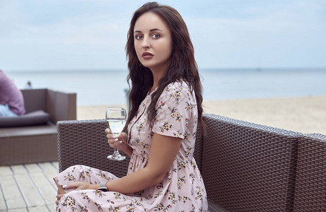 身着夏裙坐在海滩上喝着一杯白酒的年轻美丽明图片
