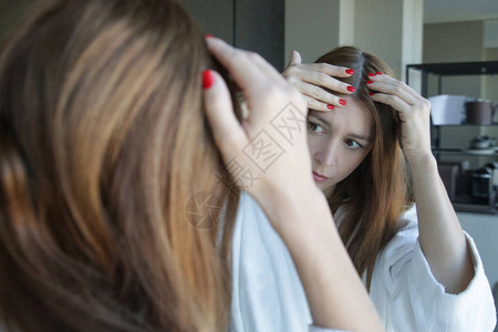 一位漂亮年轻女子在镜子前检查头皮和头发根颜色白发脱发或头皮干背景图片