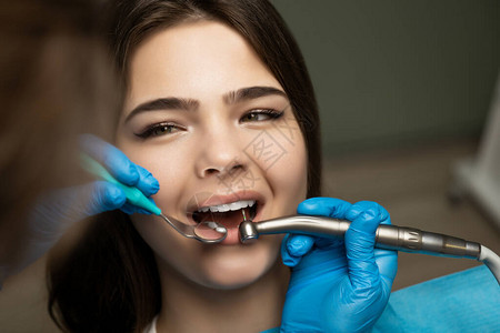 戴着蓝色手套的牙医在诊所特写医疗灯下使用镜子填充美丽微笑的女病人的根管背景图片