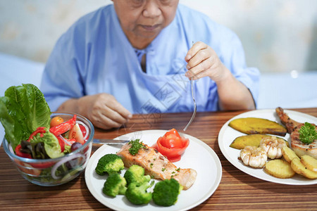 亚洲老年或老年妇人病在医院病床上坐着饿肚子吃早餐蔬菜健康食品图片