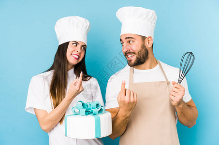年轻夫妇一起做蛋糕孤立地指着手指对着你好像邀请你更接近一样图片