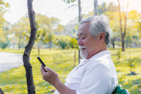 英俊的亚洲老人通过在公园使用互联网在线服务与家人进行智能手机视频通话图片